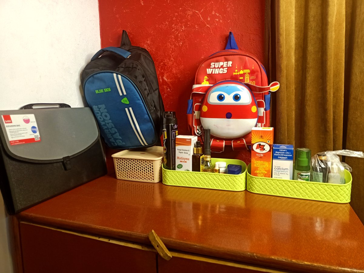 Family entryway desk after organizing — backpacks neatly stacked, daily essentials sorted into green organizer trays, medicines grouped