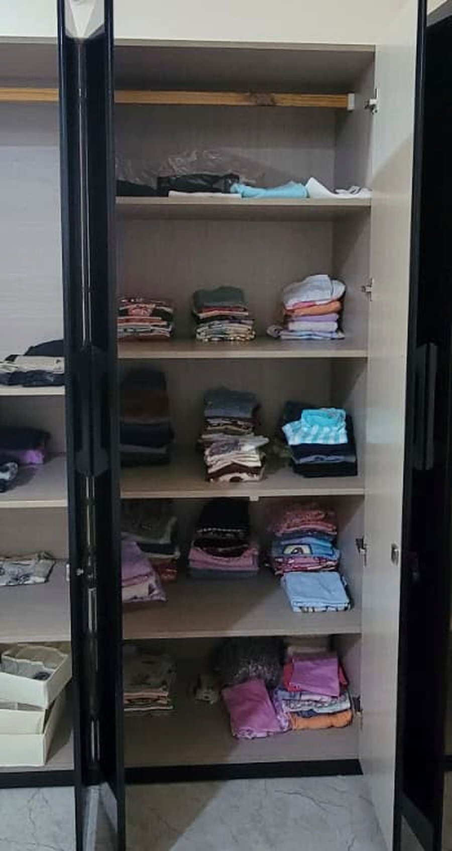 Kids wardrobe before professional organizing — folded clothes stacked on open shelves without a consistent system