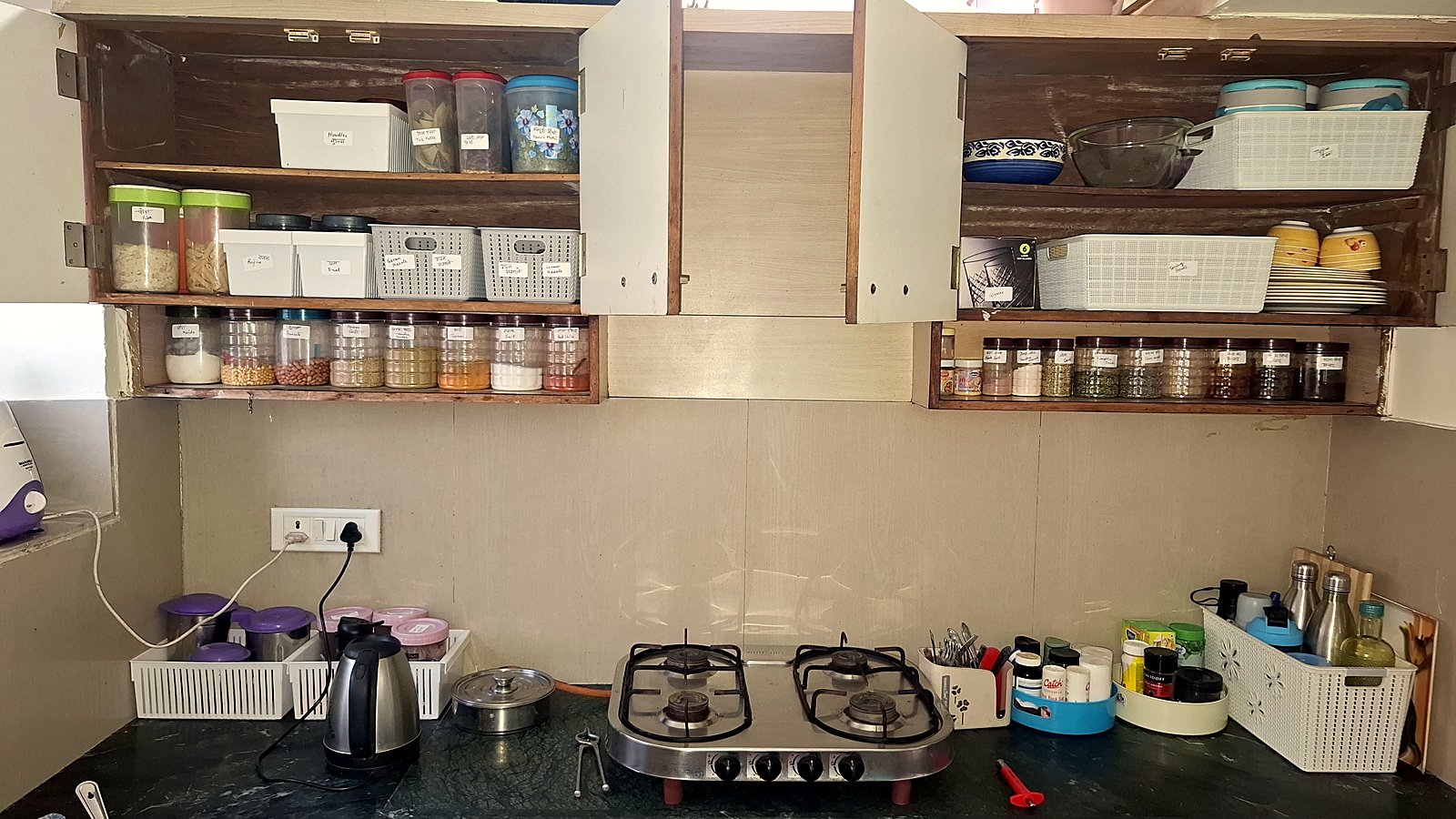 Kitchen after professional organizing — categorised labelled jars in rows, matching bins for dals and masalas, spice carousels and a zoned counter, Tulsi Nagar Indore